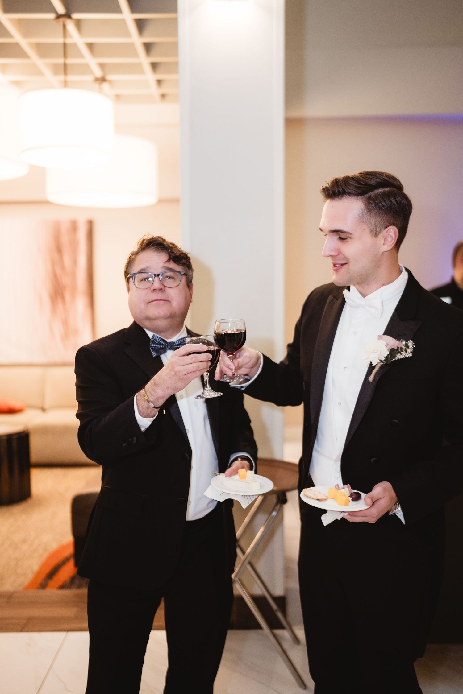 Two people in formal attire toast with wine glasses at an indoor event with warm lighting.
