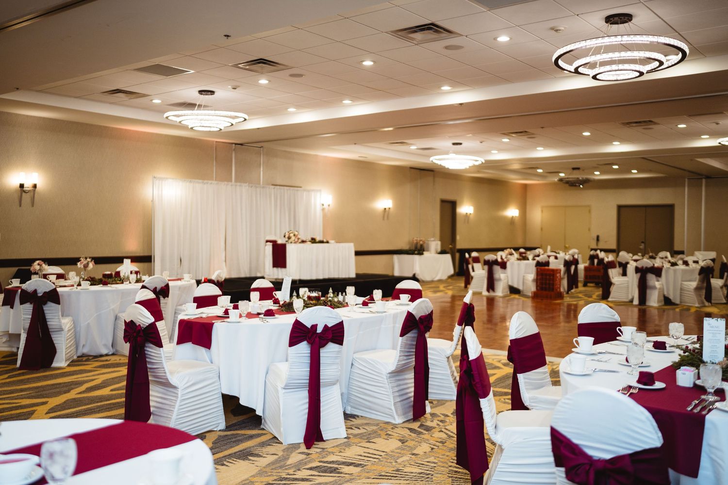 A large banquet hall decorated with white chairs and burgundy sashes, set up for an elegant wedding reception.