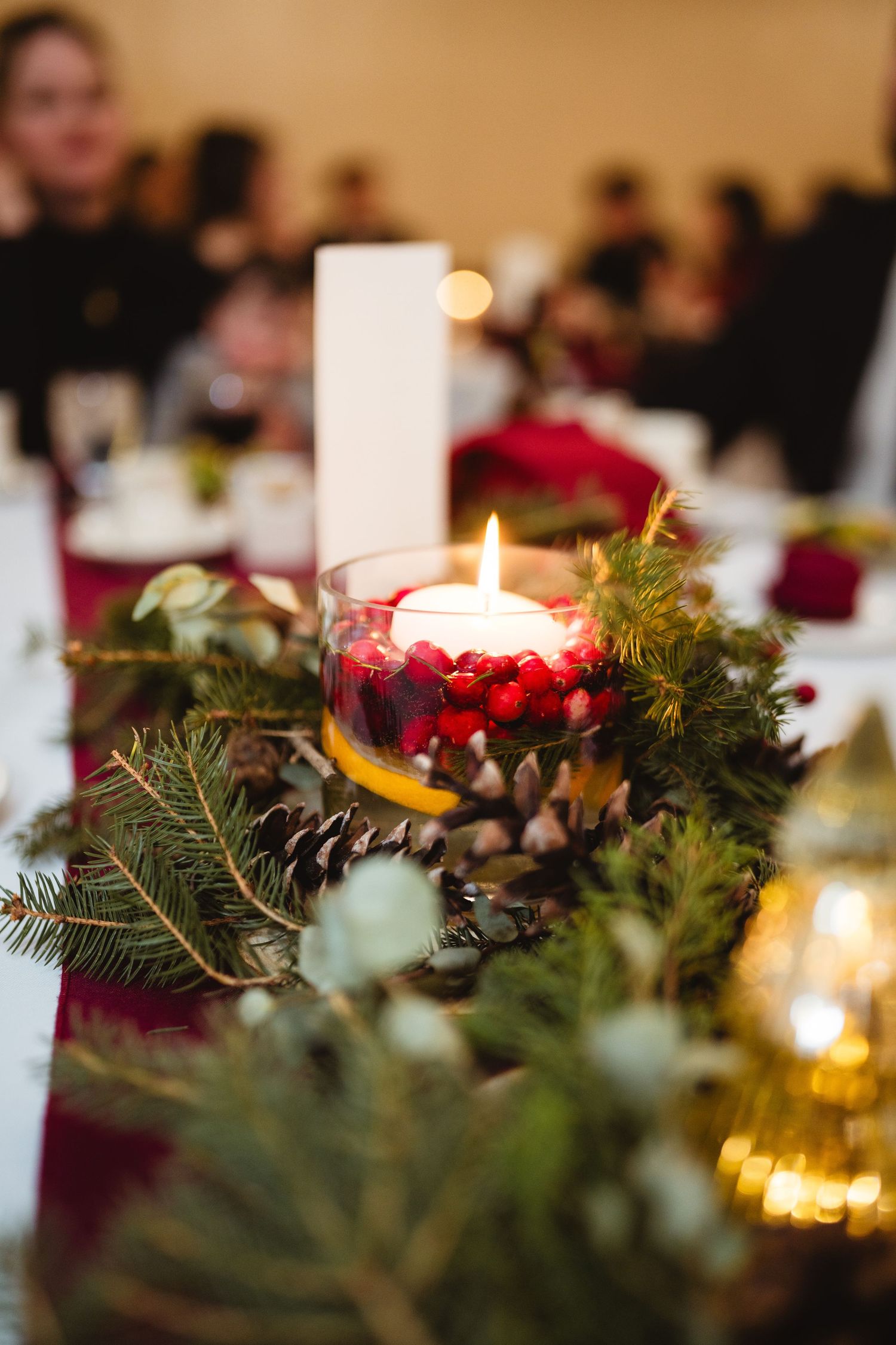 Holiday table centerpiece with evergreen branches, red berries and glowing candles.