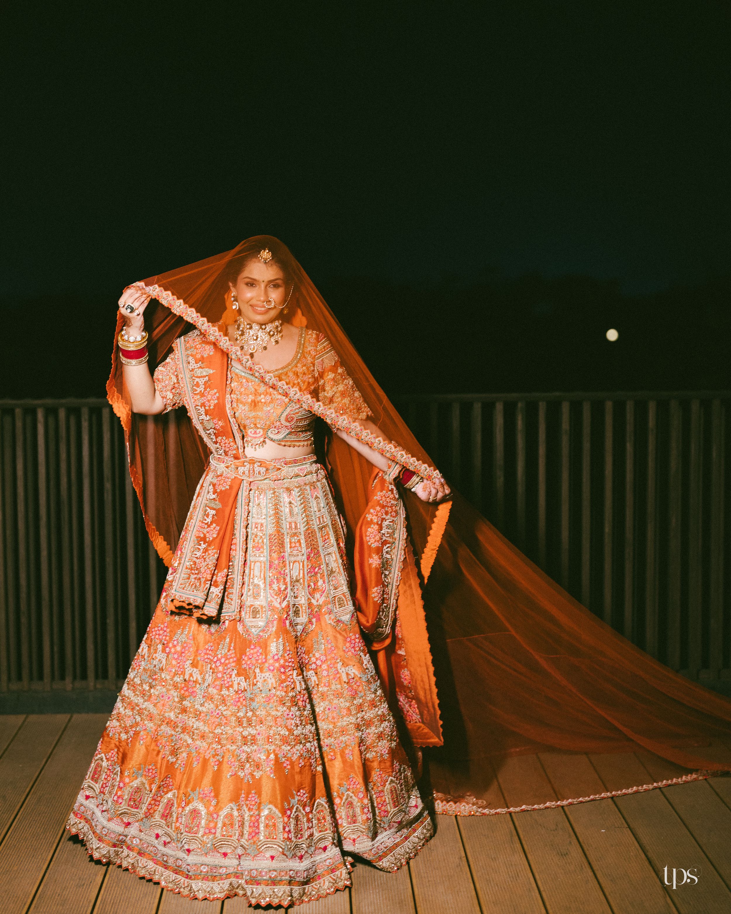 Orange & silver embellished lehenga on a wooden deck at night, beautifully captured by a professional wedding photographer in Mumbai.