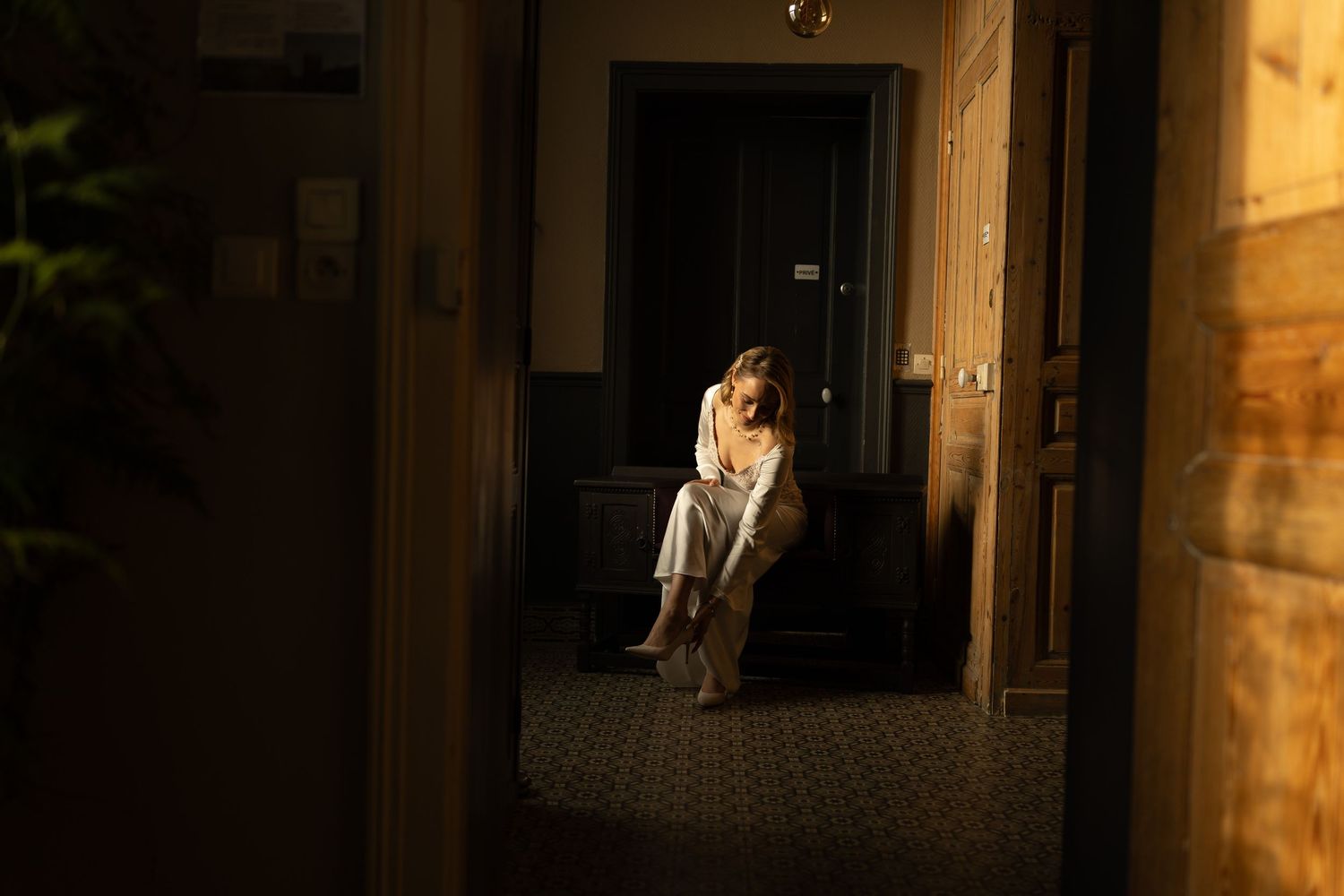 A couple in wedding attire embraces in a warmly lit doorway at night.