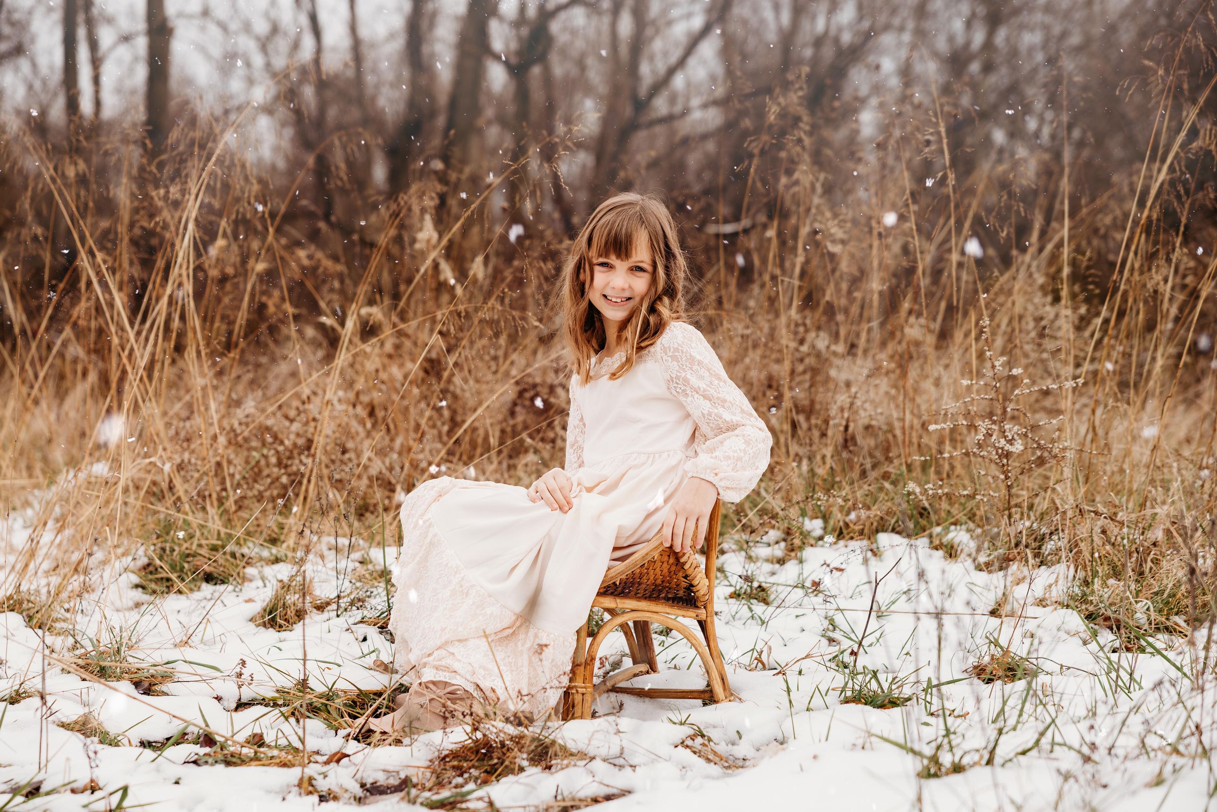 A white lace dress stands out against brown winter grass and patches of snow in a rustic outdoor setting.