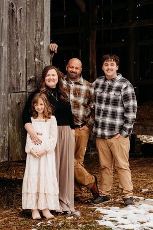 A rustic winter family portrait series showing people in plaid shirts and a pink dress against a weathered barn wall.