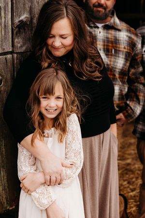Family embraces in candid moments wearing casual and lace clothing against rustic wooden backdrop.