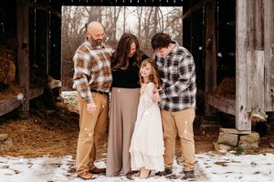 Family members in coordinating outfits share tender moments during an outdoor autumn photoshoot at a rustic barn.
