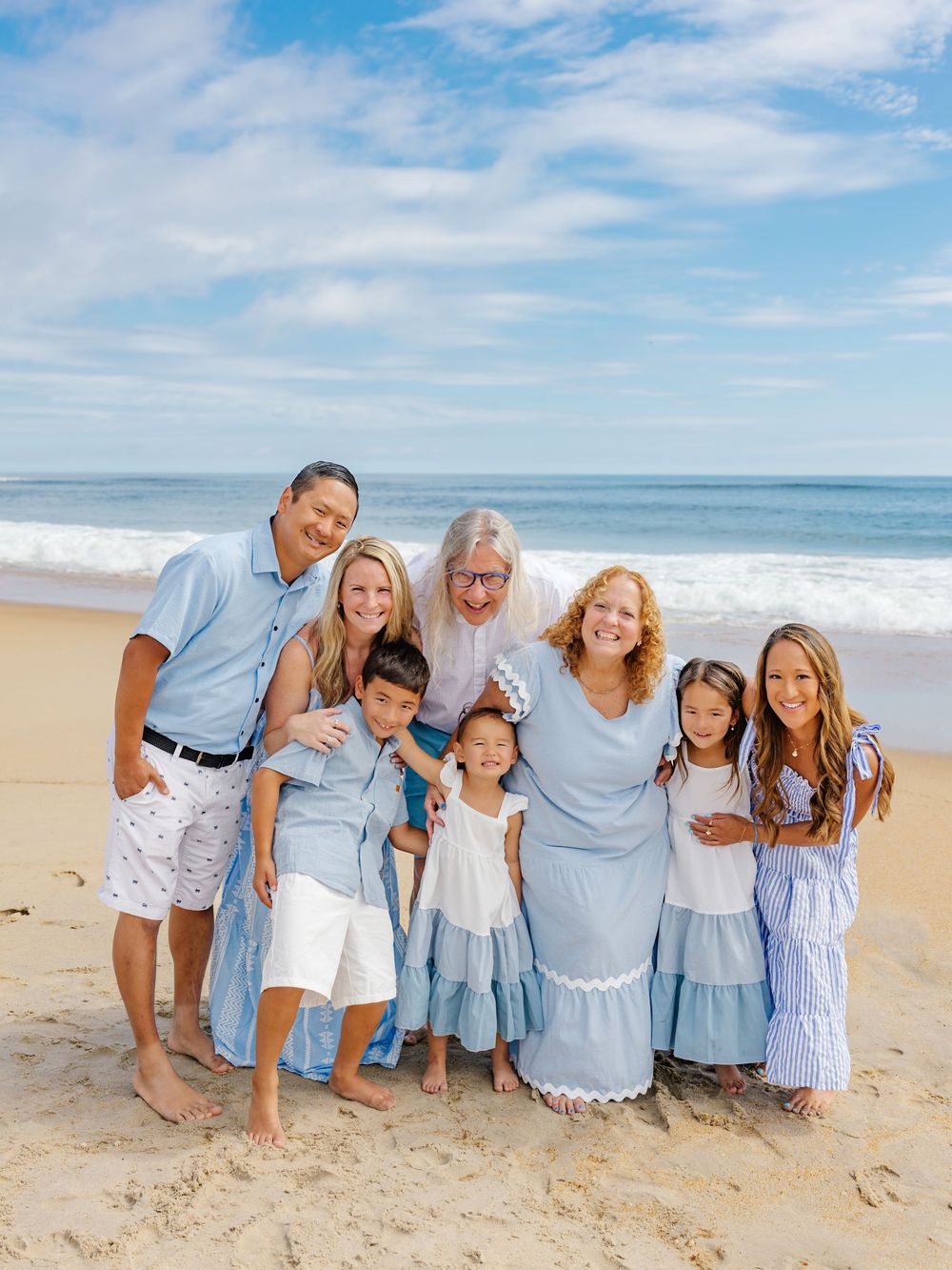 A family wearing coordinated blue and white outfits poses together on a sunny beach.