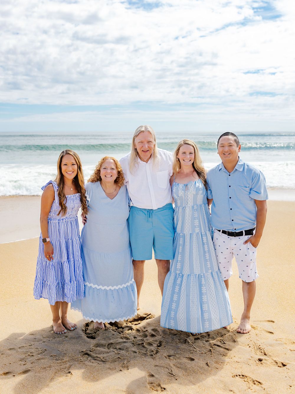 Family members in coordinated blue and white clothing pose together on a sandy beach.