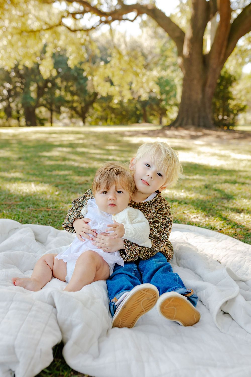 Candid family moments captured on white blanket under sunlit oak trees.