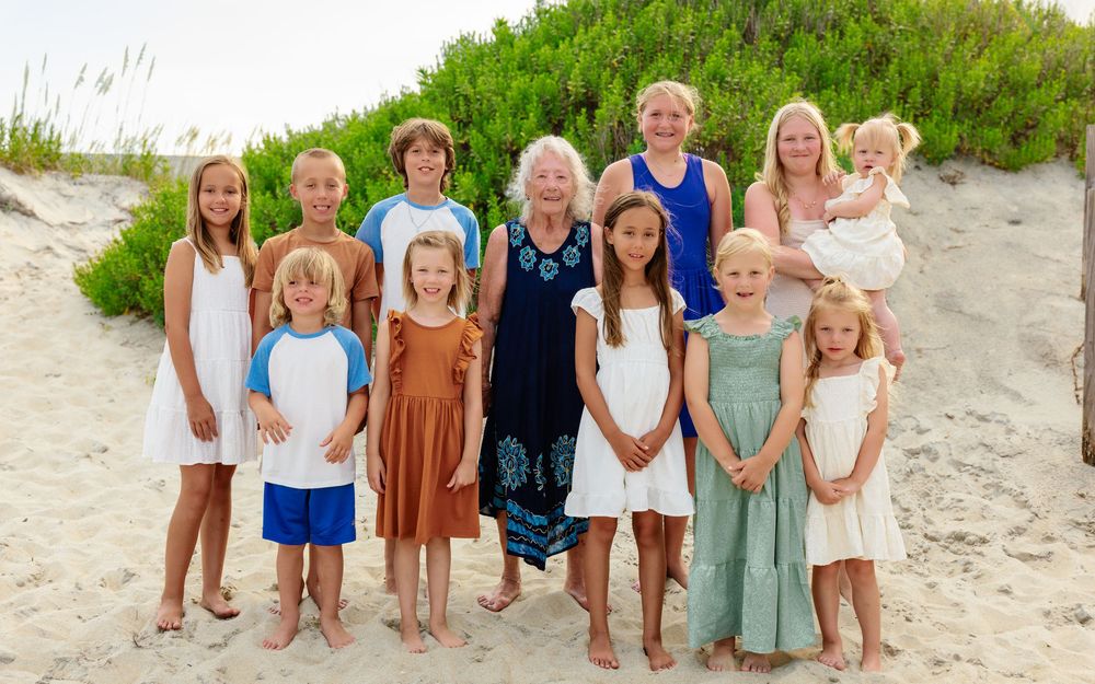 Children lined up on beach sand wearing coordinated summer outfits.