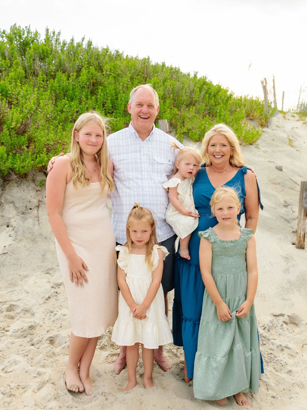 Multi-generational family group in coordinated outfits poses on sandy beach.