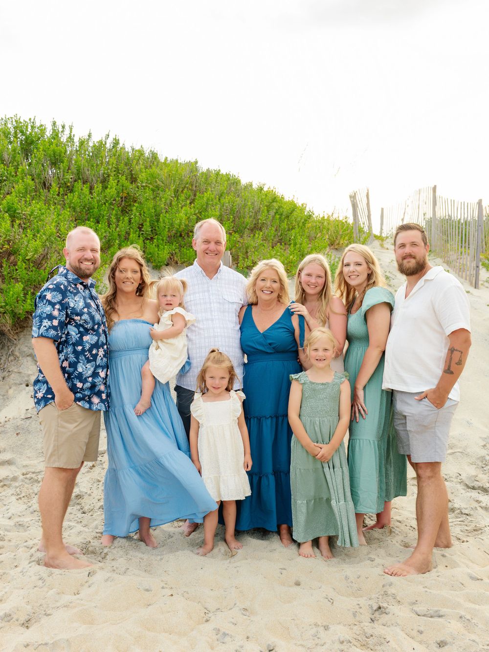 Extended family in coordinated blue and neutral tones gathered on beach dunes.