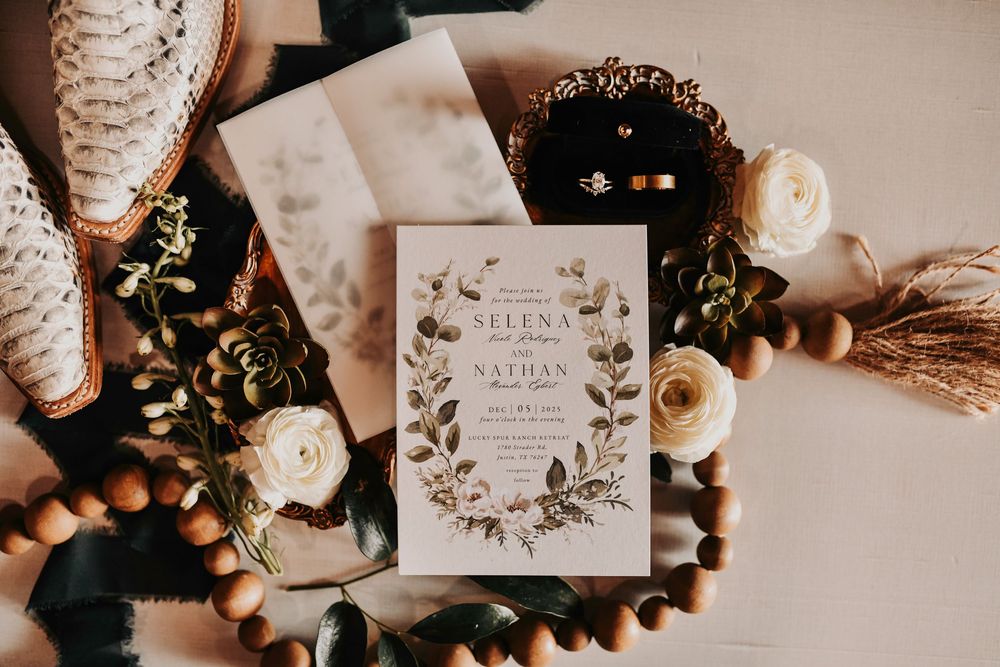 Editorial flat lay of olive-green wedding invitation suite styled with loose greenery and soft golden accents.