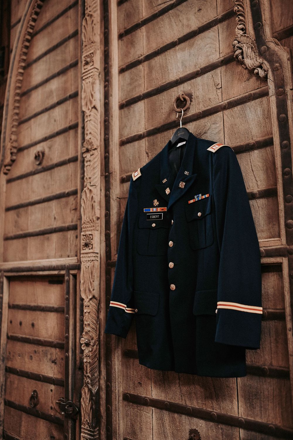 Groom’s military blues jacket hanging on rustic ranch doors in an editorial detail shot.