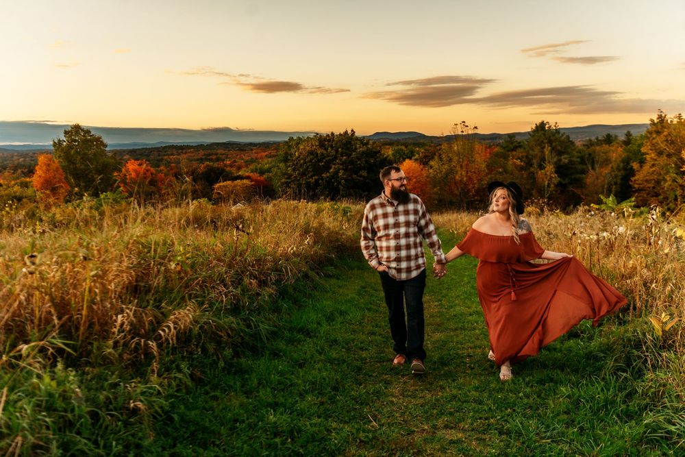 People and dogs explore a scenic hilltop meadow during golden hour with mountains on the horizon.