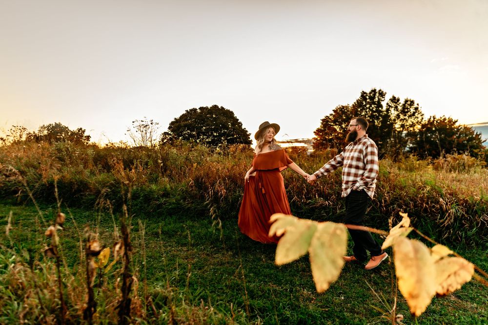 Two people enjoying a romantic moment in a hilltop meadow surrounded by autumn colors at dusk.