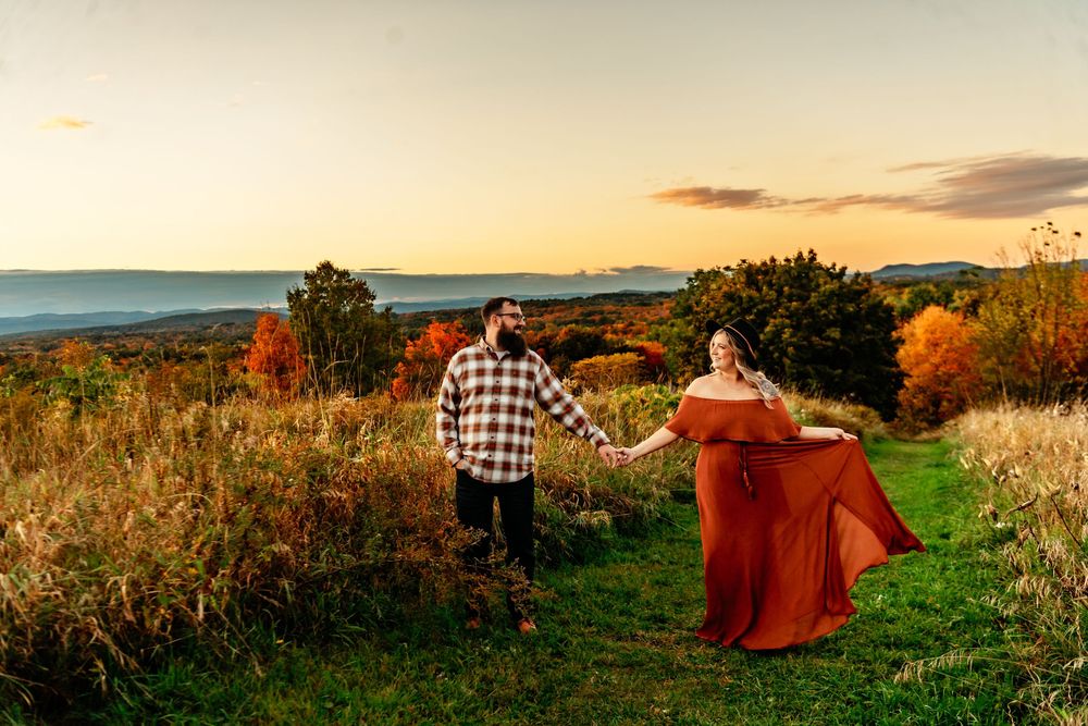 Panoramic view of a couple sitting in an autumn field at sunset with golden light and fall foliage.