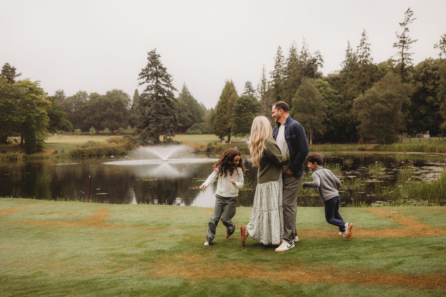 Couple walking through a serene meadow during golden hour as the sun sets behind tall evergreen trees.