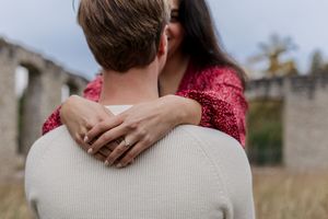 A couple embraces outdoors while wearing matching red sweaters in a romantic autumn setting.