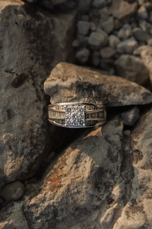 A diamond engagement ring photographed at different angles on a dark textured stone surface.