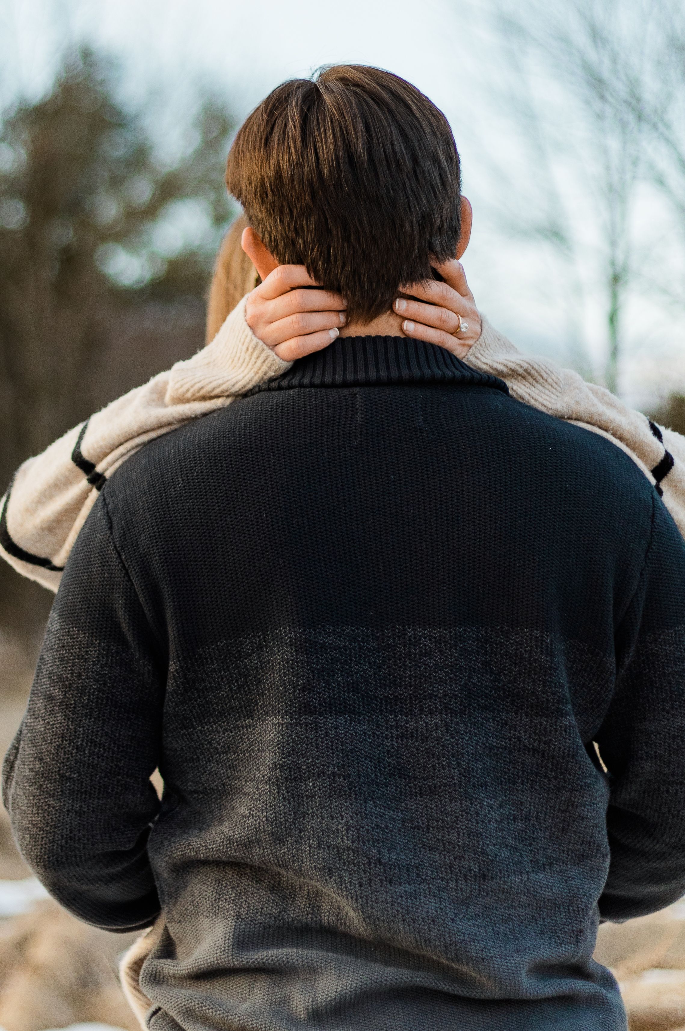 Back view of someone wearing a dark sweater receiving a neck massage outdoors on a winter day.