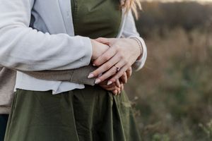 Close-up details of a bride and groom's hands showing wedding rings and formal attire during an outdoor ceremony.
