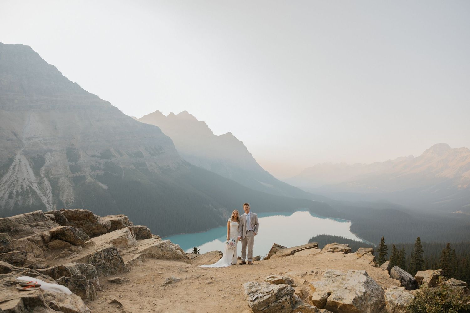 A panoramic view of a misty mountain landscape with a turquoise alpine lake nestled between snow-capped peaks.