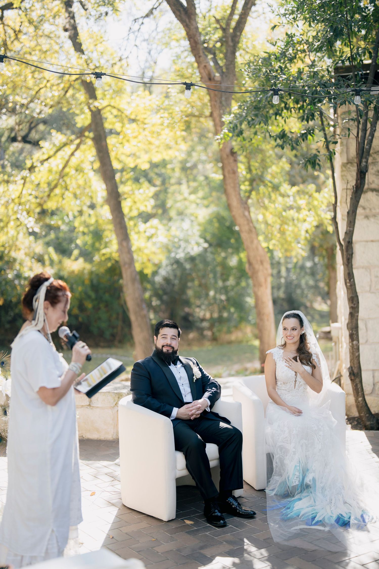 Bride and groom sitting outdoors reading together during a romantic editorial wedding photoshoot under sunlit trees.