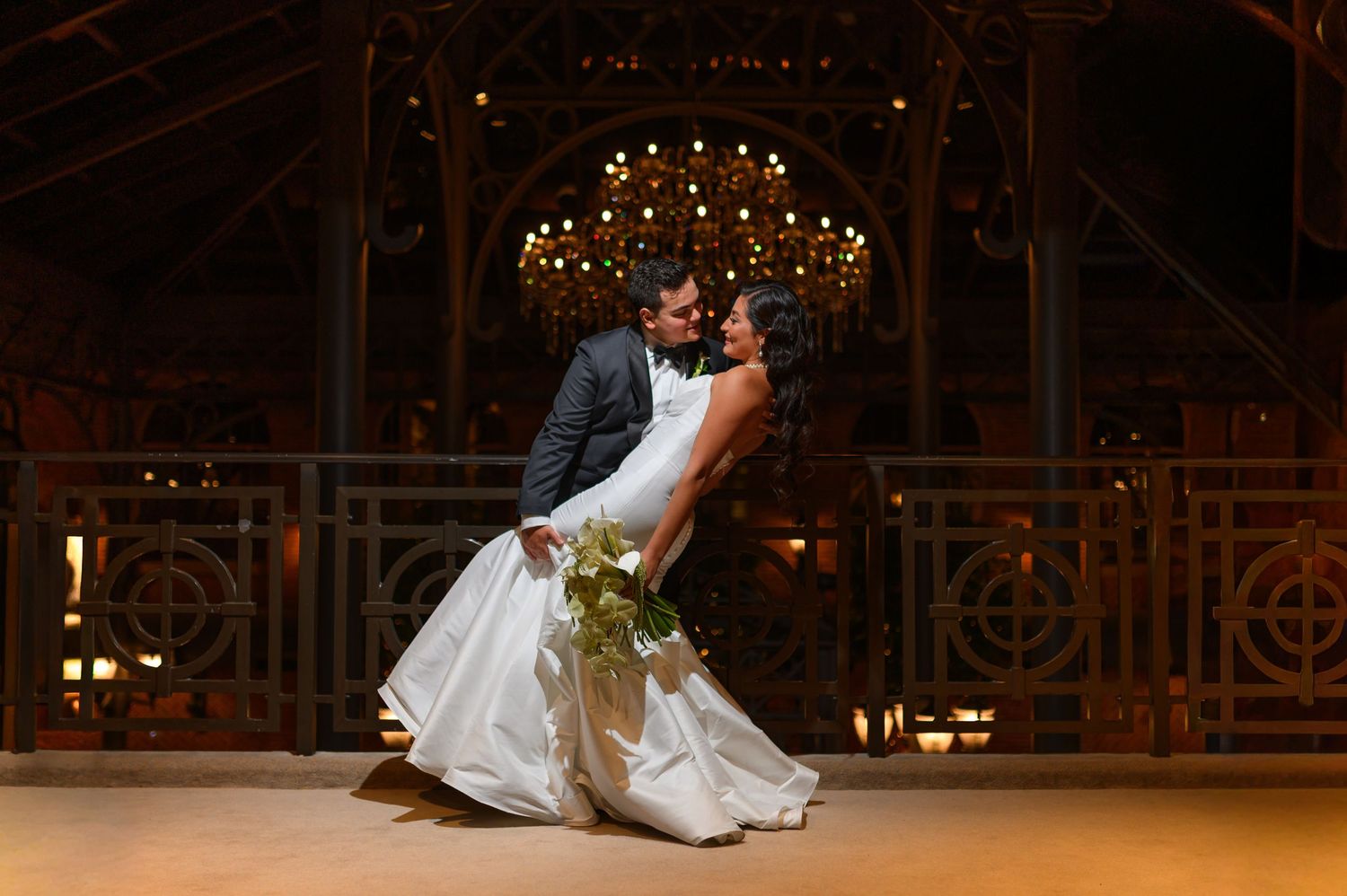 Romantic wedding couple shares intimate moments in dramatic nighttime lighting with glowing windows in background.