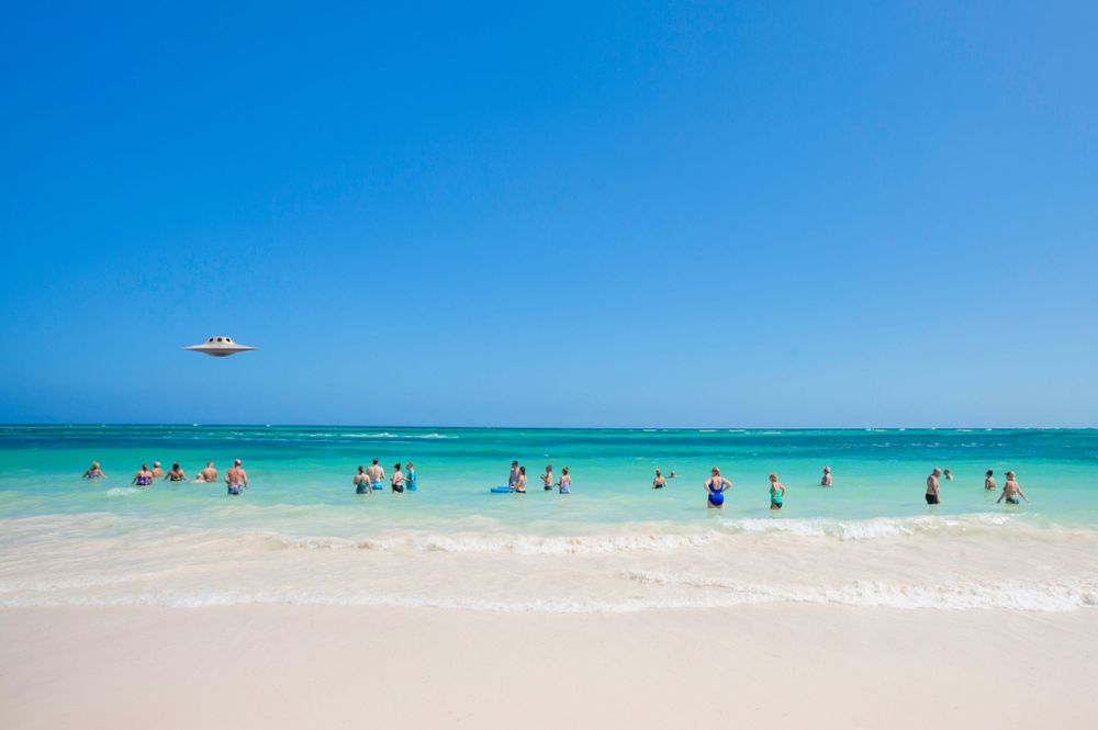 Aerial view of turquoise ocean waves meeting white sandy beach with people enjoying the tropical waters. Landscape.
