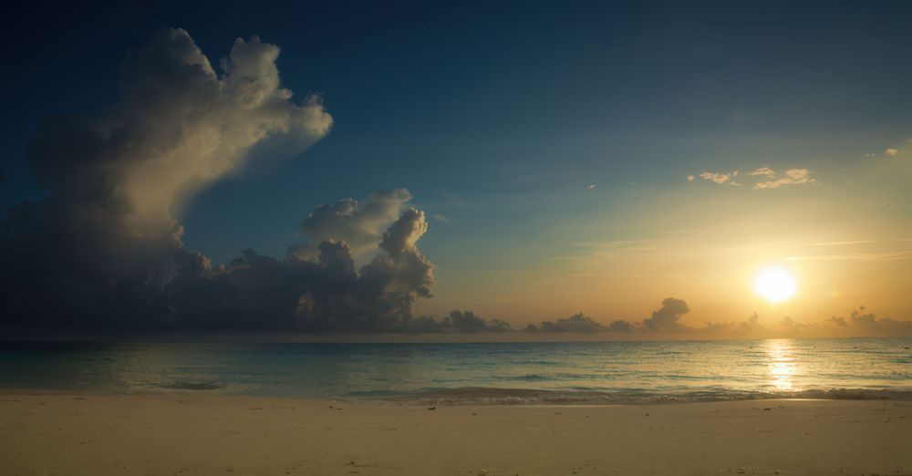 Dramatic sunset over a tranquil beach with billowing clouds and golden sunlight reflecting on calm ocean waters. Landscape.