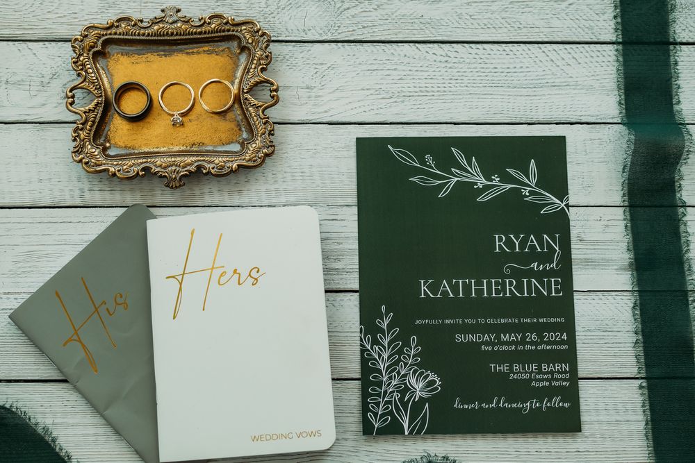 Elegant dark green and gold wedding invitations with floral designs and calligraphy on a white wooden background.