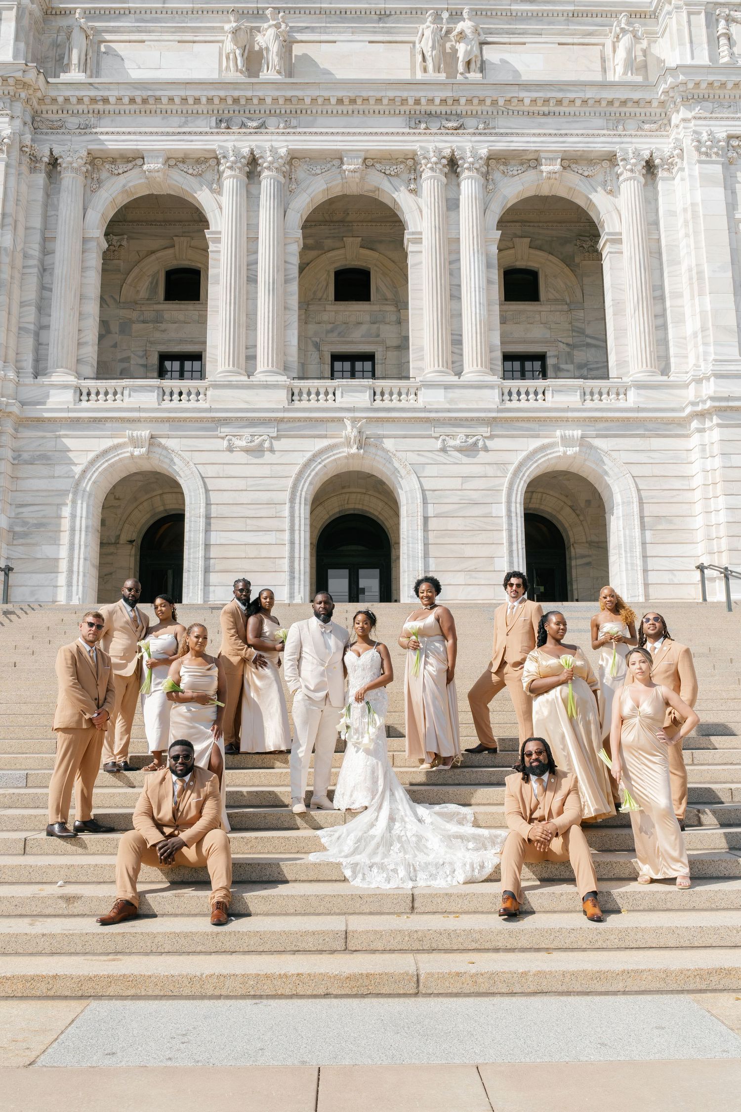 Wedding party in neutral tones posing on grand white stone steps of a historic building.