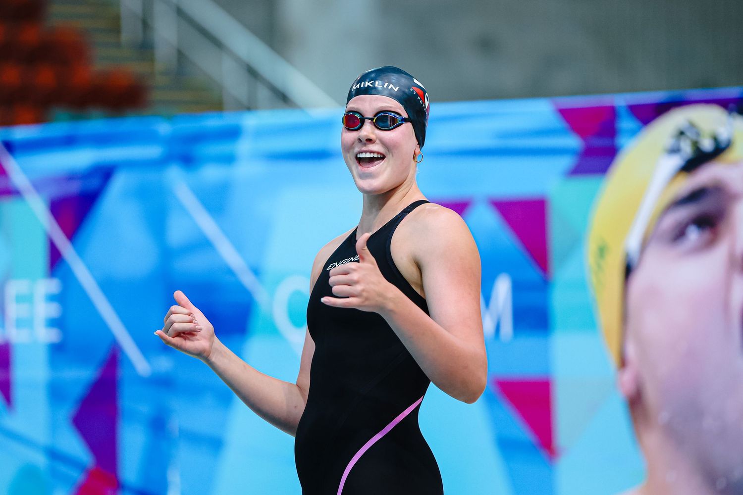 Competitive swimmer in black swimsuit and goggles celebrates with enthusiasm at swimming competition.