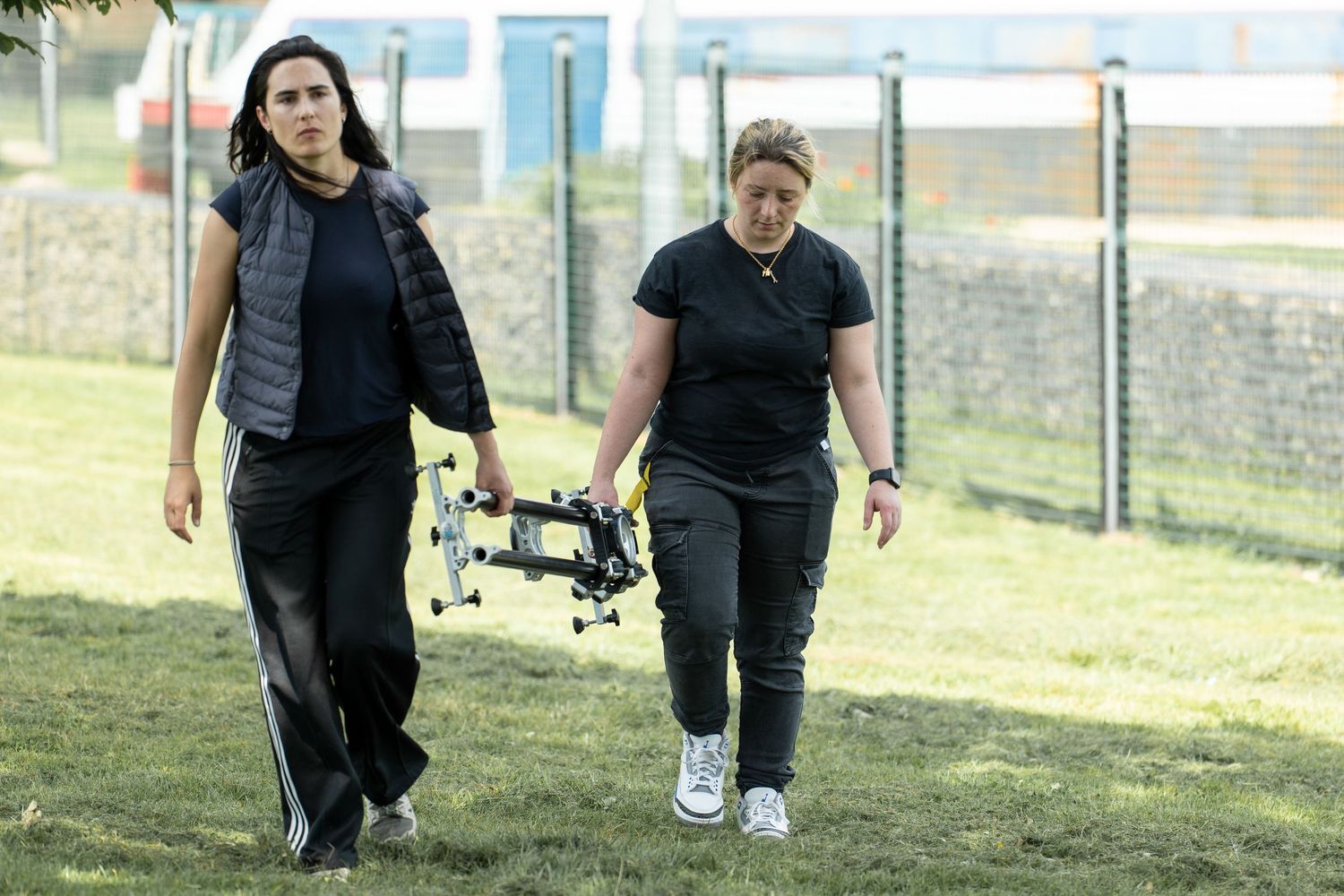 Two people walking together outdoors on grassy area near fence.