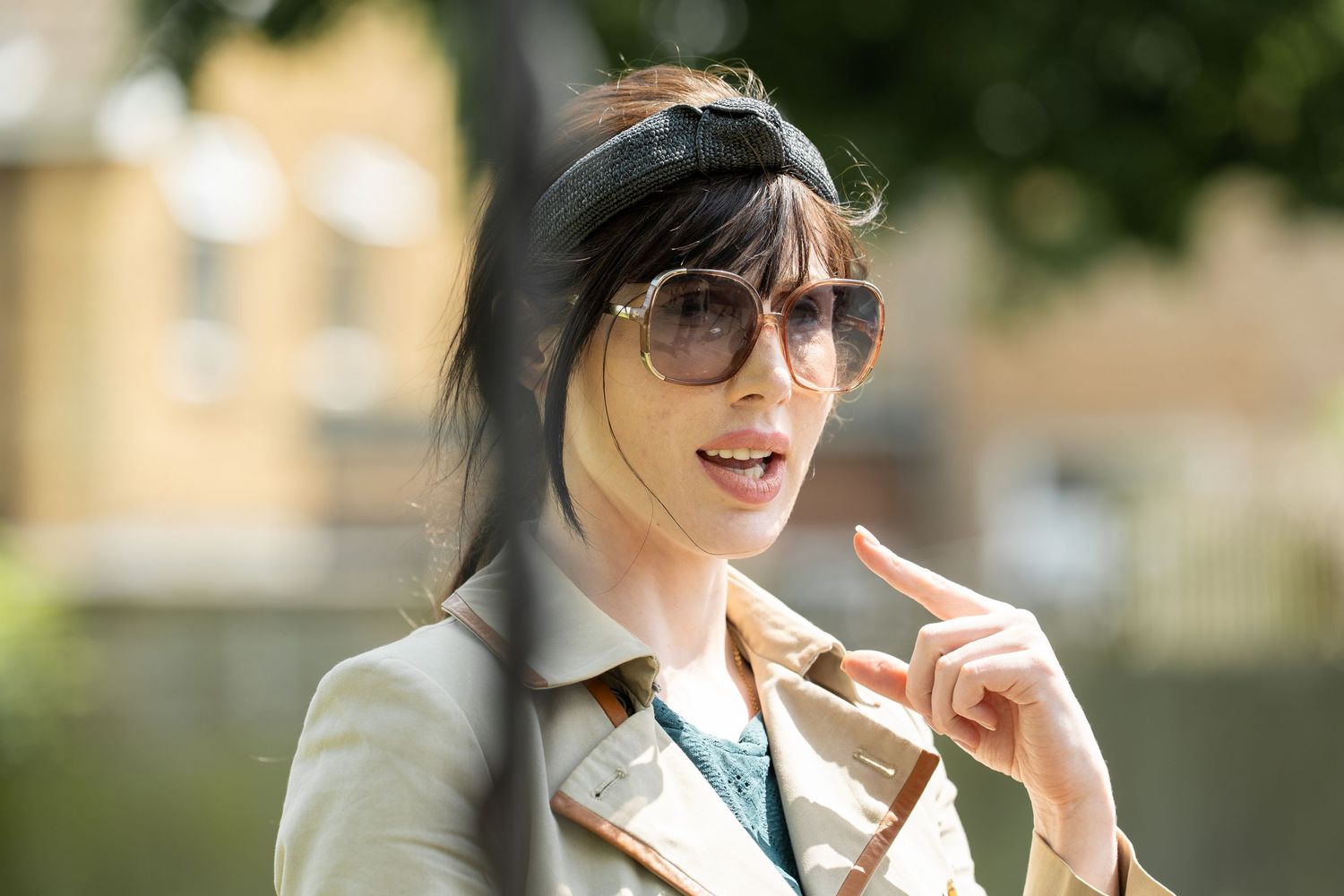 Natural portrait of a person outdoors wearing sunglasses and pointing with a beige coat on a sunny day.