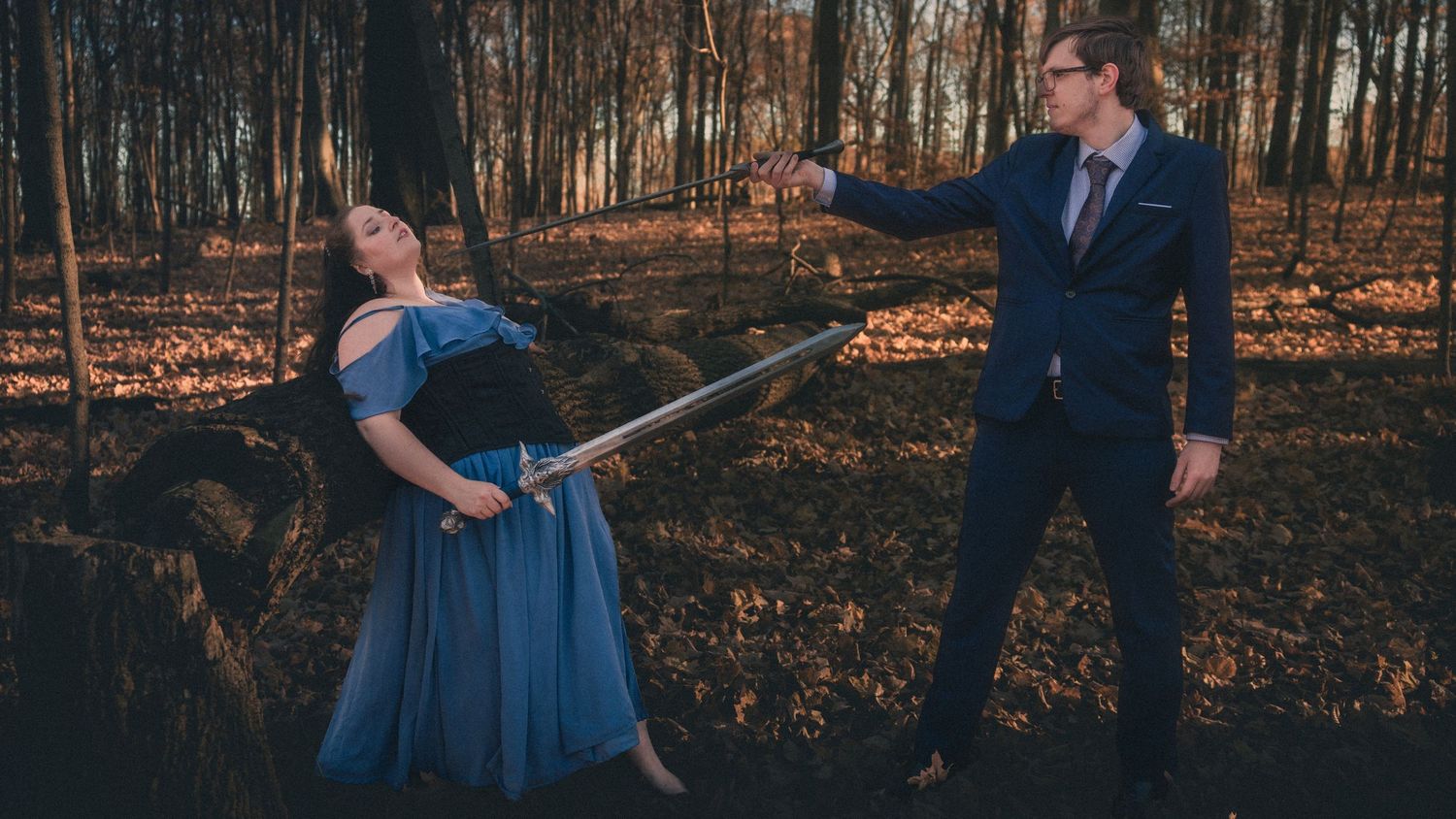 A romantic couple in blue formal attire share intimate moments during a fall forest photoshoot.