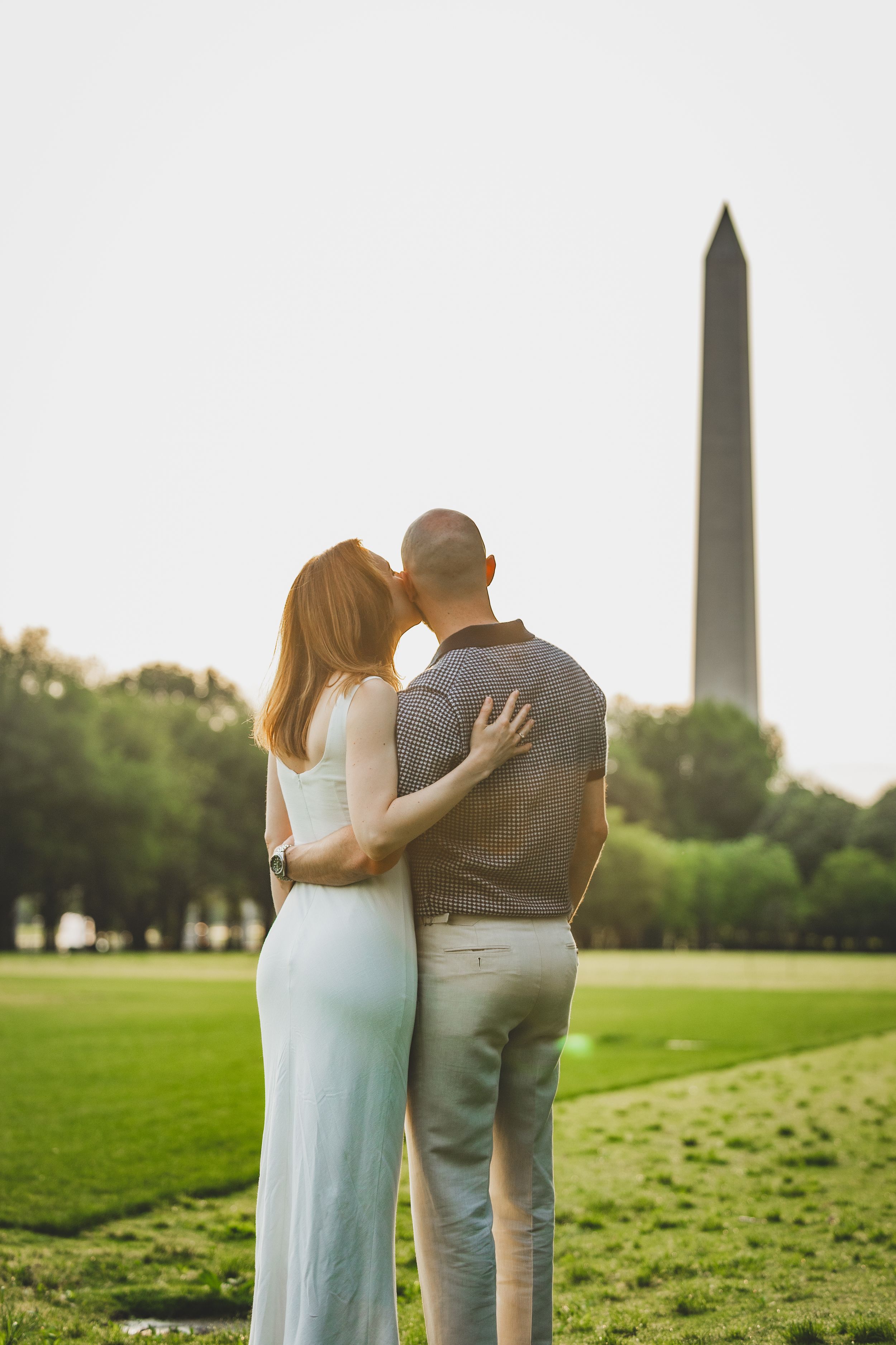 A couple embraces while looking at the Washington Monument during sunset on the National Mall in Washington DC.
