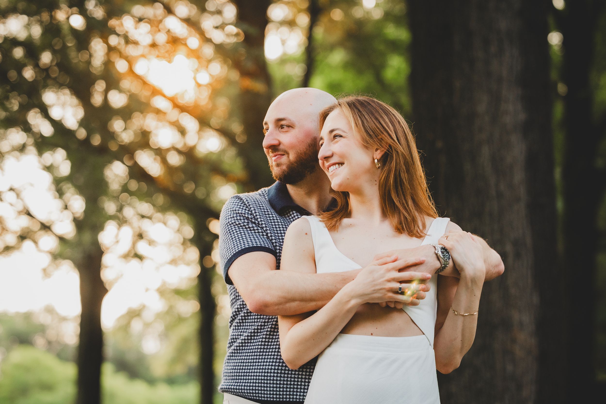 Romantic sunset engagement photos with couple embracing among tall trees in golden light.