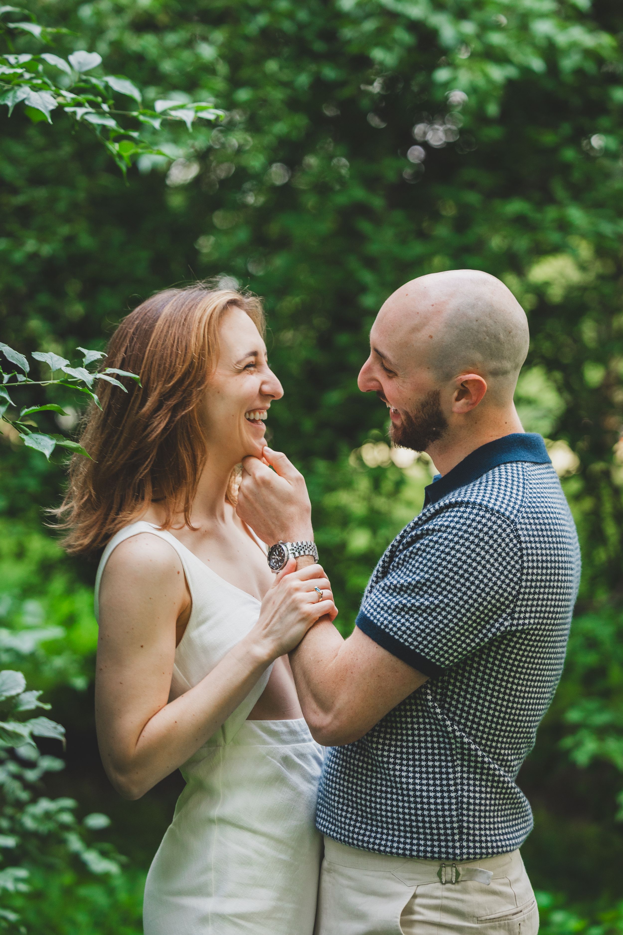 A couple laughs joyfully together in a lush green garden setting during a romantic photoshoot.