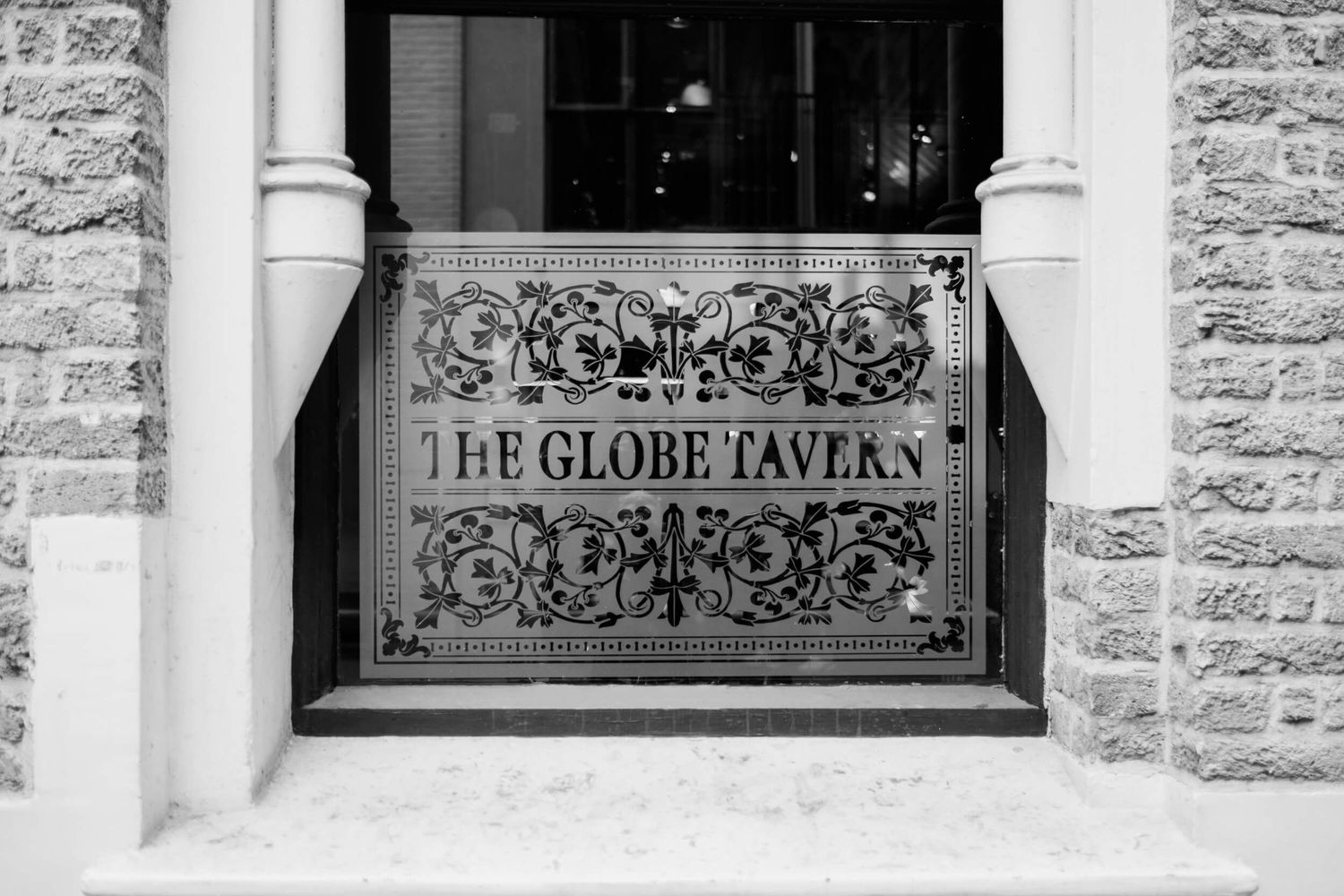 Black and white photograph of an ornate vintage window sign reading 'The Globe Tavern' with decorative scrollwork.
