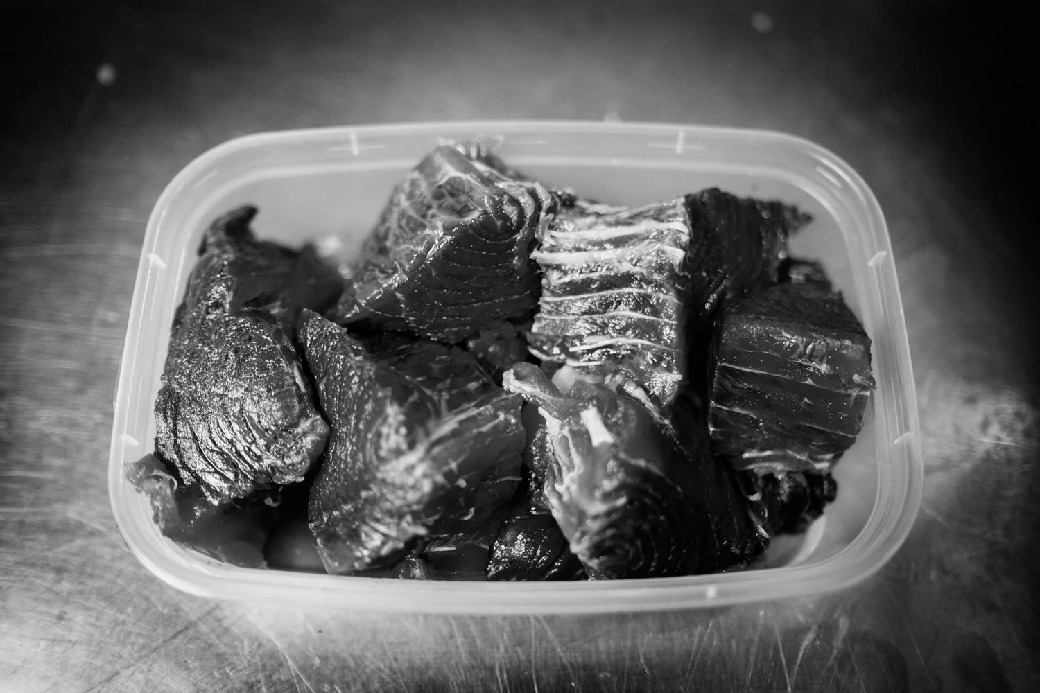 Close-up view of dark, charred meat pieces in plastic containers showing burnt edges and smoky texture.