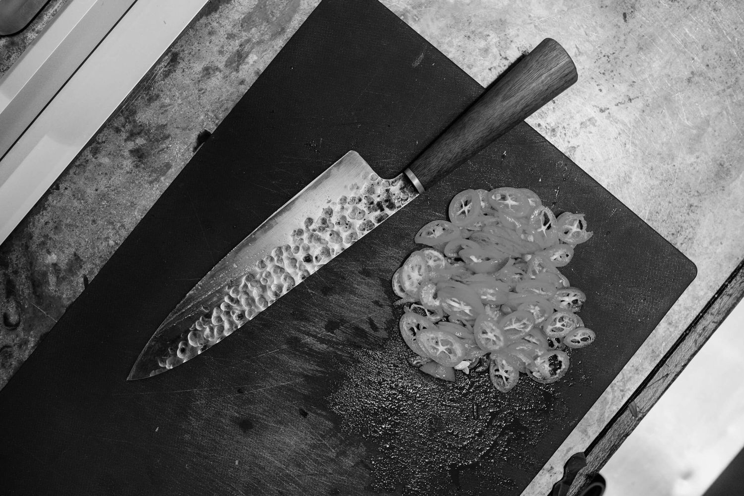Chef slicing raw fish into thin pieces on a black cutting board for sashimi preparation.