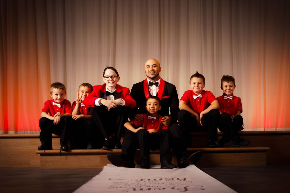 A row of performers in red and black attire seated on a stage with dramatic lighting.