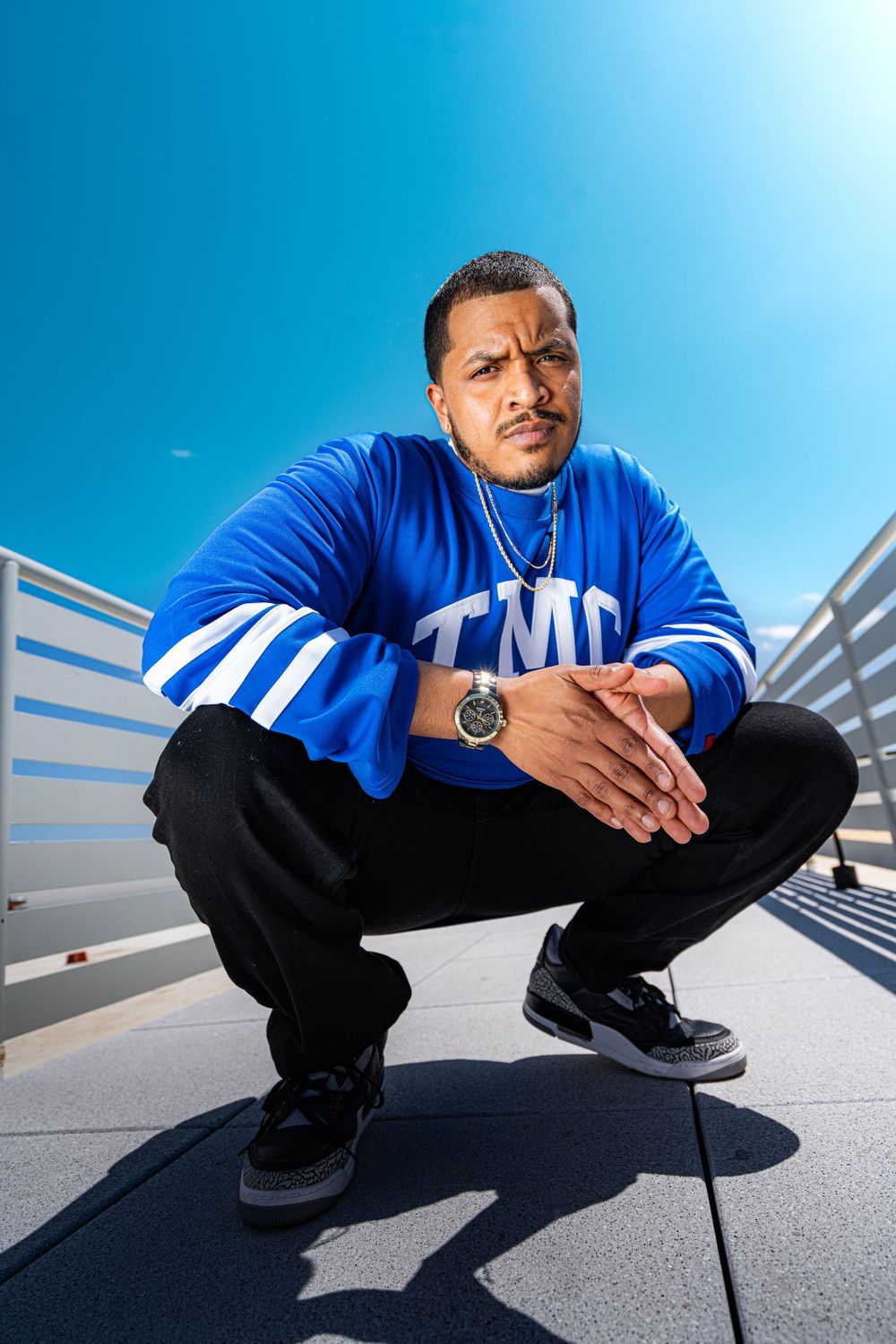 Person in a blue shirt and black pants crouches on a bright surface against a vibrant blue sky background.