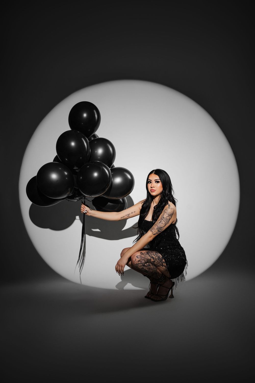 A dark artistic photo series showing a figure in black posing with black balloons against a white backdrop.