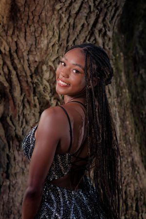Portrait of a person with braided hair wearing a sequined top against a textured tree bark background.