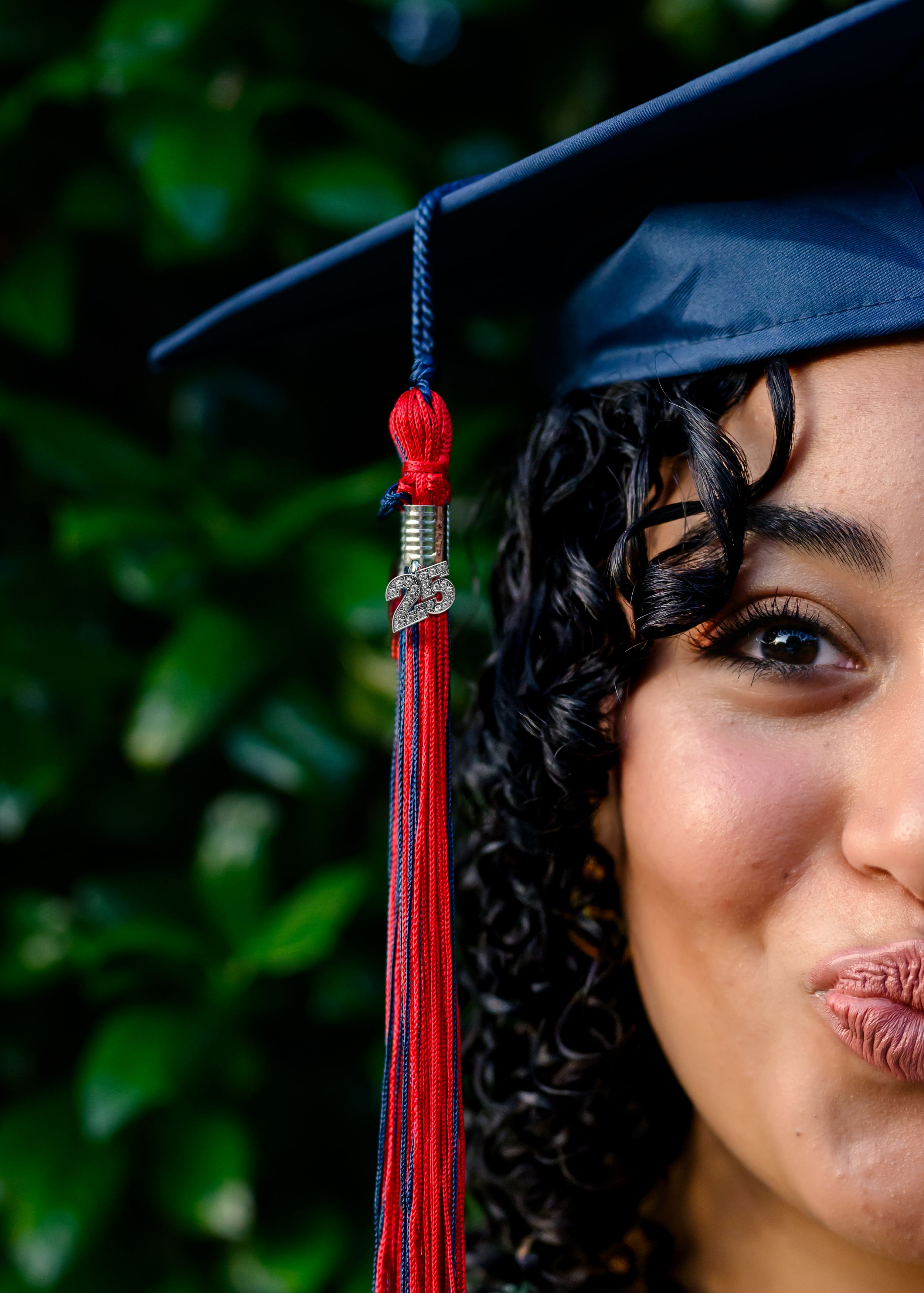 Red graduation tassel swings against a blurred green outdoor background.