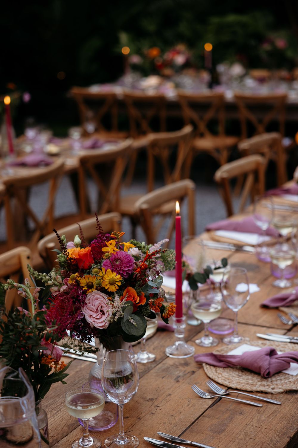 Rustic wedding table setting with vibrant floral centerpiece and wooden chairs.