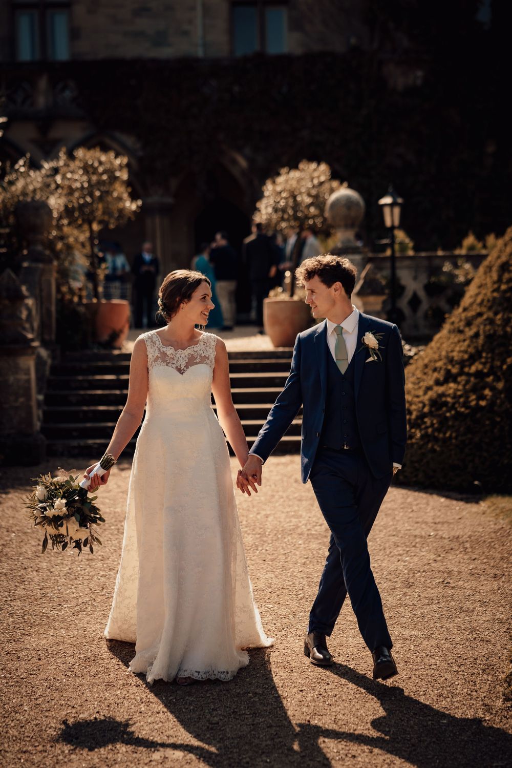 Couple walking hand in hand on gravel path during wedding photoshoot.