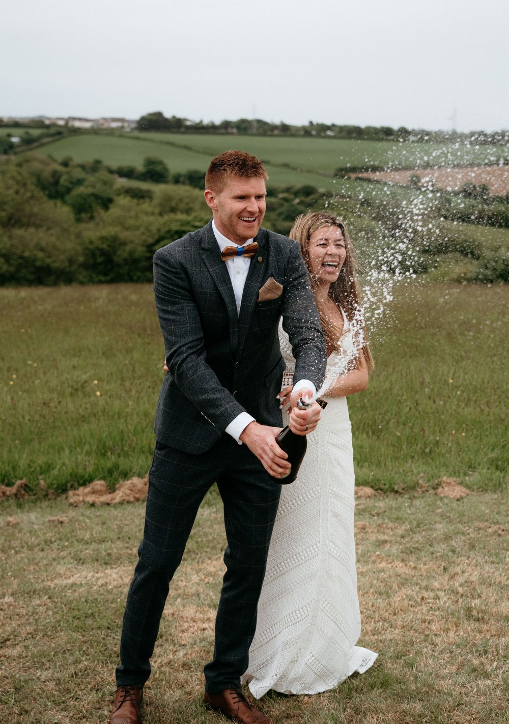 Newlyweds celebrate with champagne spray in an outdoor countryside setting.